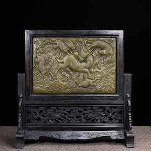 May include: A rectangular table screen featuring a central olive green stone panel with a relief carving of multiple mythical creatures amidst swirling clouds, set within a dark brown wooden frame with an intricate openwork base design.