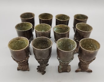 May include: Set of twelve small, antique-looking bronze cups with a green patina. Each cup has a decorative base with three feet.