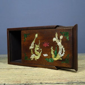 May include: A wooden box with a sliding lid, decorated with a dragon and phoenix design in mother-of-pearl inlay. The box is dark brown with a natural wood finish.