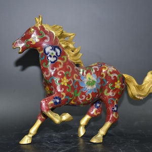 Op de afbeelding: Een rood, goud en blauw cloisonné paardenbeeldje. Het paard rent en heeft een vloeiende manen en staart. Het beeldje is versierd met ingewikkelde bloemmotieven.