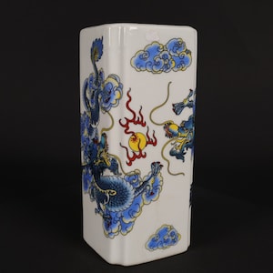 Peut inclure: Un vase rectangulaire blanc orné d'un motif de dragon bleu détaillé. Le dragon est entouré de nuages bleus et d'accents jaunes. Des flammes rouges et un soleil jaune complètent l'œuvre d'art d'inspiration asiatique.