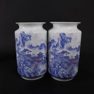 Pode incluir: Dois vasos de porcelana branca com desenhos pintados em azul e vermelho de uma paisagem chinesa com montanhas, árvores e um edifício.