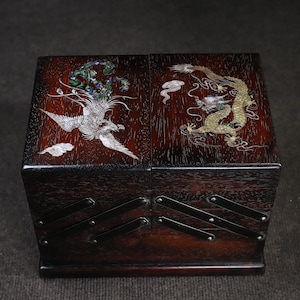 May include: A wooden box with a hinged lid, decorated with inlaid mother-of-pearl designs of a phoenix and a dragon. The box has metal accents and a dark wood finish.