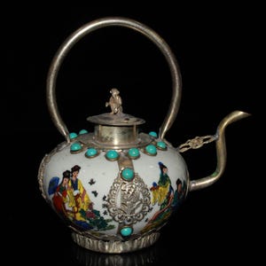 Könnte beinhalten: Eine verzierte weiße Teekanne mit silbernem Griff und Ausguss. Die Teekanne ist mit türkisfarbenen Steinen und farbenfrohen gemalten Szenen von Figuren verziert. Eine kleine Affenfigur sitzt auf dem Deckel.