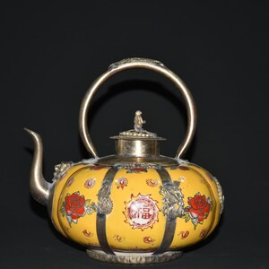 May include: A yellow ceramic teapot with a silver handle, spout, and lid. The teapot is decorated with red roses, silver accents, and Chinese characters. The teapot has a round shape.
