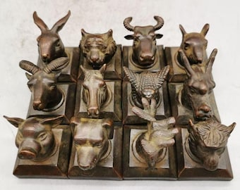 Puede incluir: Una colección de doce esculturas de cabezas de animales en tono bronce, cada una montada sobre una base cuadrada. El conjunto presenta varias criaturas, incluyendo un conejo, tigre, buey, rata, cabra, caballo, serpiente, dragón, cerdo, perro, gallo y mono.