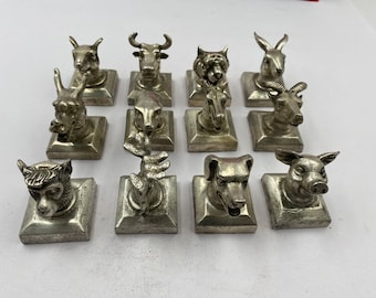 May include: Twelve silver animal figurines on square bases. The animals include a bull, a deer, a pig, a monkey, a dog, a rabbit, a goat, a bird, and a few others.