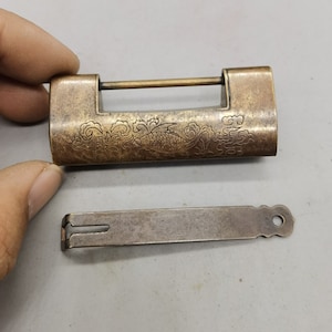 Op de afbeelding: Een antiek messing hangslot met een ingewikkeld ontwerp van een vis en bloemmotieven. Het hangslot wordt geleverd met een bijpassende sleutel.