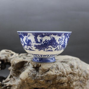 May include: A white porcelain bowl with a blue and white design. The bowl features a scene of a man riding in a chariot pulled by a tiger. The bowl has a small foot.