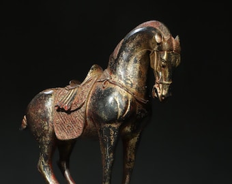 Puede incluir: Una escultura de caballo de bronce con una silla de montar y una brida. El caballo está de pie sobre una superficie de madera y tiene una pátina marrón oscura.