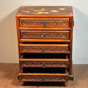 Puede incluir: Un cofre de madera de cinco cajones con intrincados tallados y un diseño floral en la parte superior. Los cajones están todos abiertos, revelando el interior.