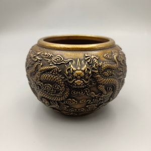 May include: A small, round, brass incense burner with intricate carvings of dragons and clouds. The burner has a dark, aged patina.