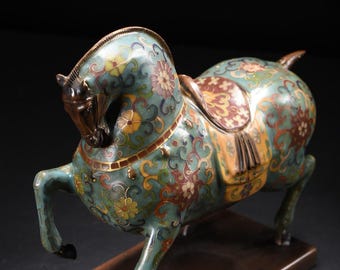Puede incluir: Figura decorativa de caballo con un patrón floral turquesa y dorado. El caballo tiene una silla de montar y está montado sobre una base rectangular. La figura es de metal y tiene un diseño detallado.