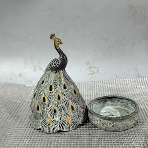 May include: A bronze peacock incense burner with a detailed design. The burner is open and the lid is separate. The peacock is depicted with a spread tail and intricate details.