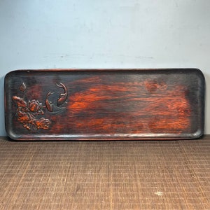 Può includere: Un vassoio di legno lungo e rettangolare con una finitura marrone rossiccio scuro. Il vassoio ha un design intagliato di un fiore di loto e due pesci su un'estremità.