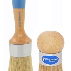 May include: Two paint brushes with light wood handles and natural bristles. The left brush has a long handle with a blue top and the text Chalk Mountain. The right brush has a round knob handle and a silver band with the text Chalk Mountain Brushes.