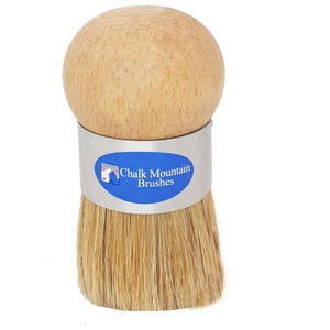 May include: A wooden handled brush with natural bristles. The brush has a silver band with the text "Chalk Mountain Brushes" in blue.
