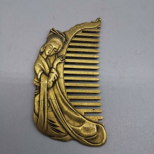 Könnte beinhalten: Ein goldfarbener Kamm mit einem detaillierten Design einer Frau in einem traditionellen japanischen Kimono. Der Kamm hat einen dekorativen Griff und eine Reihe von Zähnen.