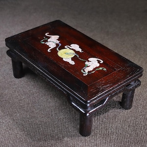 May include: A dark wood table with four legs and a rectangular top. The top is inlaid with a design of clouds and a circle, made of mother of pearl.