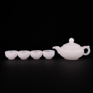 Könnte beinhalten: Ein weißes Keramik-Tee-Set mit einer Teekanne und vier Tassen. Die Teekanne hat einen runden Körper mit einem Deckel und einem Ausguss. Die Tassen sind klein und rund.
