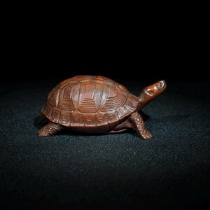 Op de afbeelding: Een gedetailleerd houten beeldje van een schildpad, met een bruine afwerking. De schildpad loopt vooruit met zijn kop omhoog.