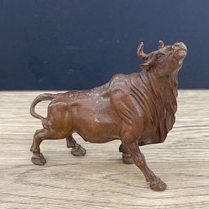 Puede incluir: Una escultura de bronce de un toro con la cabeza echada hacia atrás y la boca abierta. El toro está de pie sobre sus cuatro patas y tiene una apariencia detallada y realista.