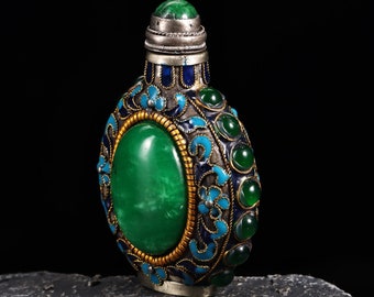 May include: A small, round, green jade bottle with silver and blue enamel detailing. The bottle has a silver cap and is decorated with floral motifs.