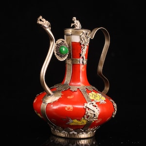 Könnte beinhalten: Eine rote Keramik-Teekanne mit silbernen Akzenten und floralen Designs. Die Teekanne hat einen drachenförmigen Ausguss und eine Affenfigur auf dem Deckel.