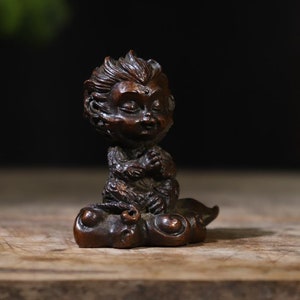 May include: A small, dark brown wooden sculpture of a monkey sitting on a cloud. The monkey has a detailed face and is holding its hands together in prayer.