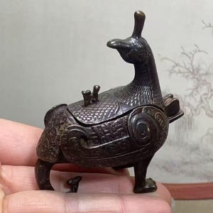 May include: A bronze incense burner shaped like a stylised bird, featuring intricate details and a removable lid.