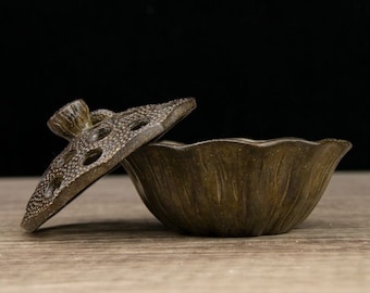May include: A brown ceramic incense burner shaped like a lotus flower with a lid that has holes in it. The lid is open and the burner is sitting on a wooden surface.