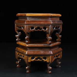 May include: A two-tiered wooden stand with an octagonal top and intricate carvings. The stand is made of dark brown wood and has a traditional Chinese design.