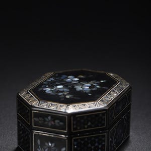 May include: An octagonal black box featuring intricate mother-of-pearl floral inlays on the lid and sides. The lid displays a detailed flower cluster, while the sides are decorated with geometric patterns and small floral motifs in iridescent tones.