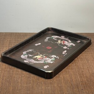 May include: A rectangular wooden tray with a dark brown finish. The tray features a painted design of two dragons in a circle with a red dot in the centre. The dragons are white with gold and green accents.