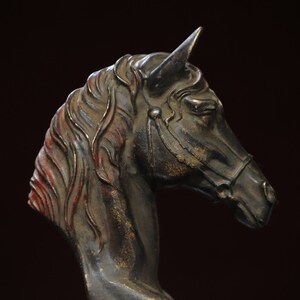 Op de afbeelding: Een donkerbruin paardenkopbeeld met een getextureerd oppervlak en gouden accenten. Het beeld is gemaakt van metaal en heeft een gedetailleerde manen en hoofdstel.