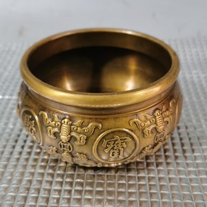 May include: A small, round, brass bowl with intricate carvings and Chinese characters. The bowl has a golden color and a smooth, polished finish.