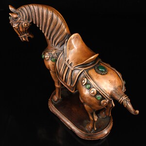 May include: A bronze horse statue with green gemstone accents. The horse is standing on a base and has a saddle with intricate details.