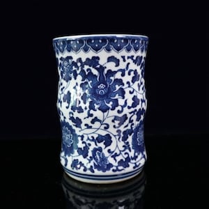 Puede incluir: Un jarrón de cerámica blanca con un patrón floral azul y blanco. El jarrón tiene una parte superior ligeramente acampanada y una base redondeada.