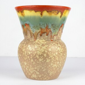 以下が含まれることがあります： 斑点のあるベージュのボディとカラフルな釉薬を施したセラミックの花瓶。釉薬は、赤、黄、緑、青の色合いの滴り落ちる効果があります。