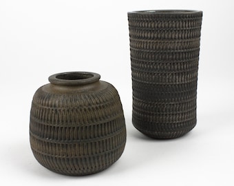 May include: Two ceramic vases with a woven pattern. The vase on the left is round and the vase on the right is cylindrical. Both vases are a dark brown color.