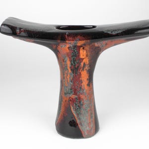 Peut inclure: Un vase en céramique noire avec une forme abstraite unique et une large ouverture plate. Le vase a un glaçage marbré avec des nuances d'orange, de rouge et de vert.