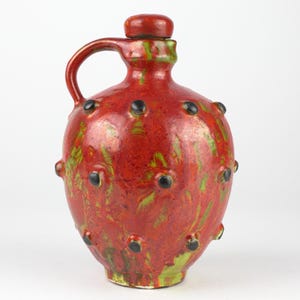 May include: A red ceramic jug with a handle and a stopper. The jug is adorned with black and green accents. The jug is approximately 10 inches tall.