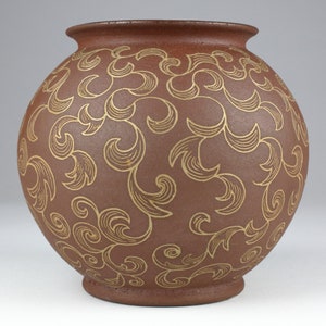 Può includere: Un vaso rotondo in ceramica marrone con un motivo a spirale dorato.