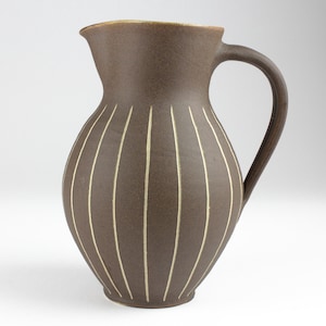 May include: A brown ceramic pitcher with a white stripe design. The pitcher has a wide base and a narrow neck with a handle.