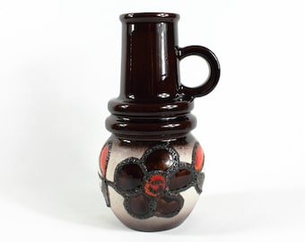 May include: A brown ceramic vase with a handle and a floral design. The vase has a white background with brown and red flowers.