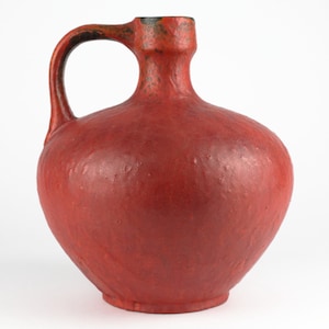 Puede incluir: Una jarra de cerámica roja con una superficie texturizada y un asa.