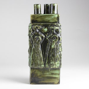 May include: A green ceramic vase with a textured surface and two spouts. The vase features a raised design of two figures with long flowing robes.