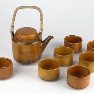 May include: A brown ceramic teapot with a bamboo handle and six matching cups. The teapot and cups have a mottled brown glaze.