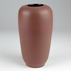 Puede incluir: Un jarrón alto y cilíndrico con un acabado liso y mate. El jarrón es de color marrón rojizo oscuro con un borde negro.