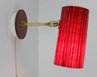 May include: A red, ribbed, cylindrical lampshade attached to a brass wall sconce with a wooden base.